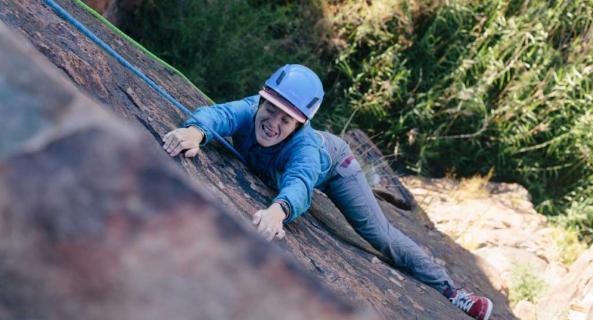 a person climbing a rock wall makes a silly face at the camera